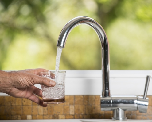 photo d'un avant bras avec un verre qui est en cours de remplissage à un robinet